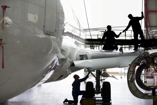 inside of a hanger where 3 men are working on a large airplane, two of the men are standing on the wing